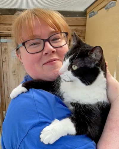 red-haired woman with glasses wearing blue t-shirt and holding black-and-white cat