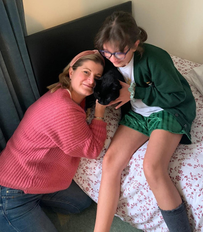 blonde woman and brunette schoolgirl cuddling black cat on bed