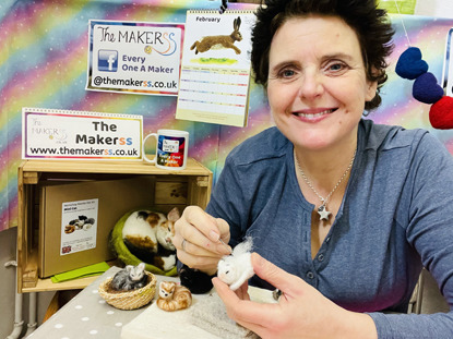 short-haired brunette woman in blue top needle felting a cat