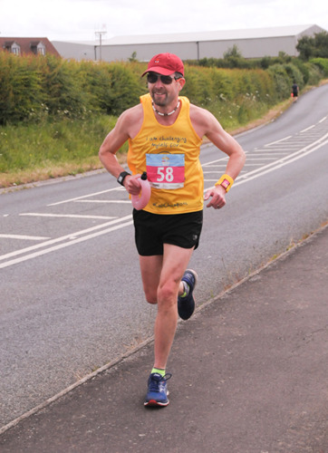 man wearing yellow Cats Protection running vest running along pavement