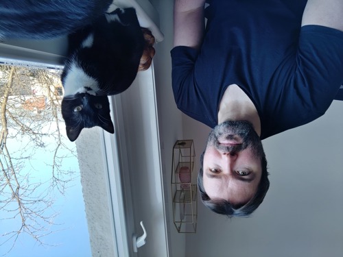 short-haired man with beard next to black-and-white cat on windowsill