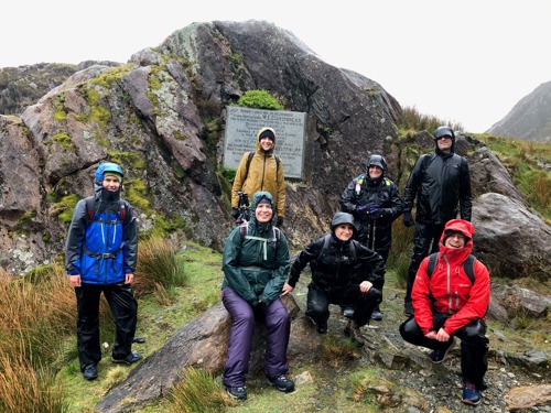 Group of people wearing raincoats standing in front of large rock